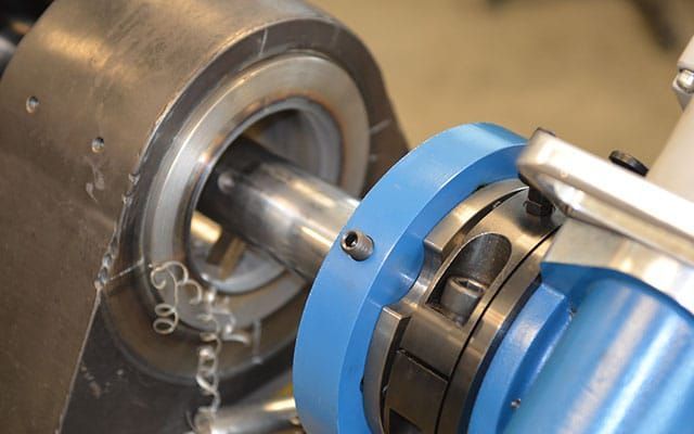 A metal rod being machined by a blue and silver lathe, with metal shavings visible.