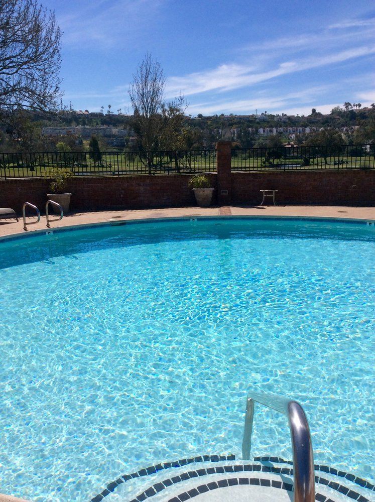 A large swimming pool is surrounded by a fence on a sunny day.
