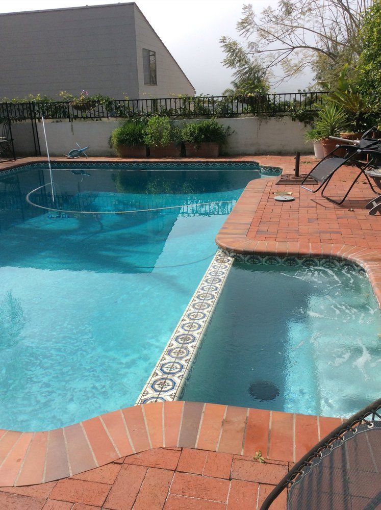 A large swimming pool is surrounded by a brick patio
