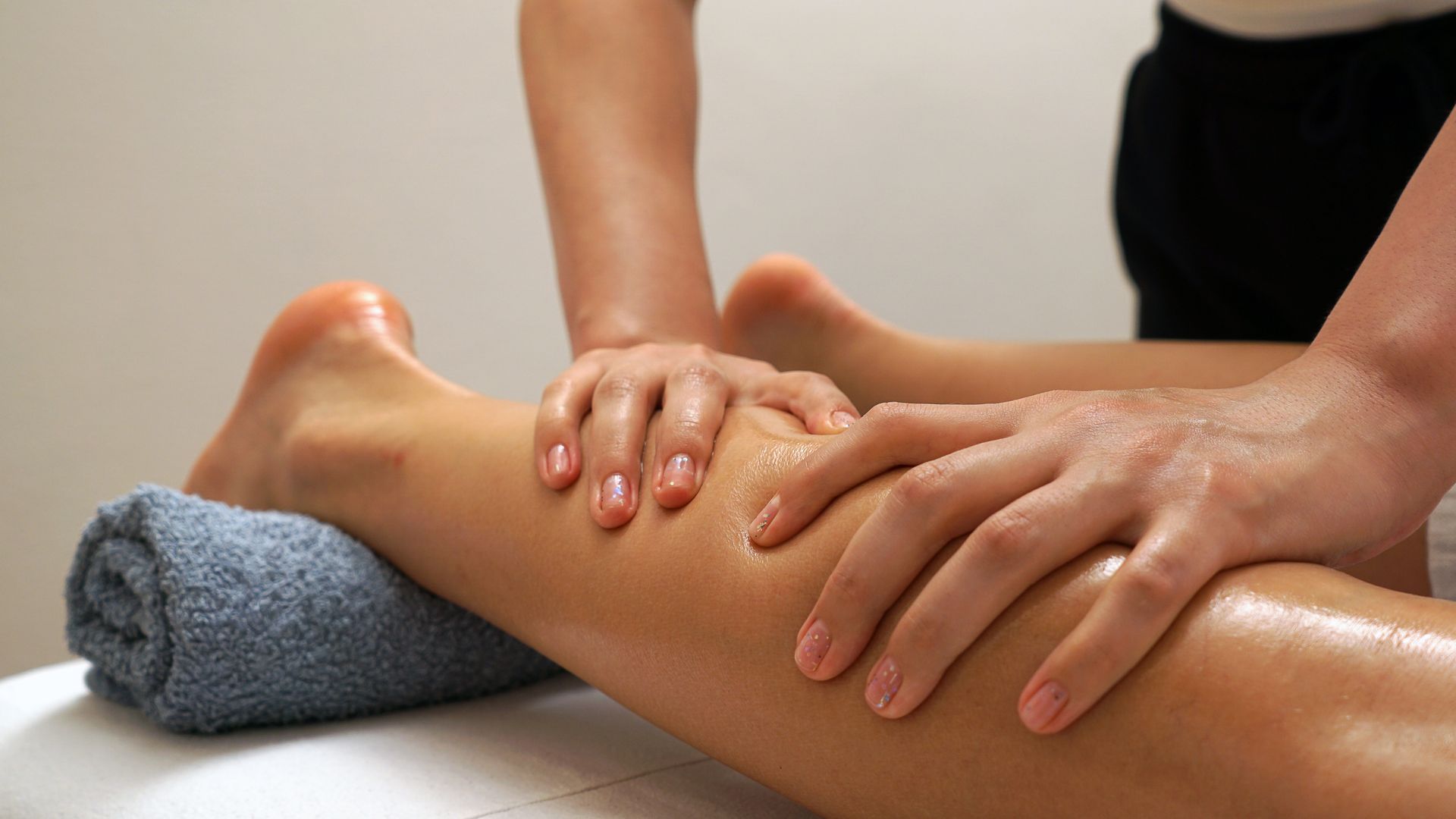 Massage therapist kneading a client's leg with a rolled towel under the ankle