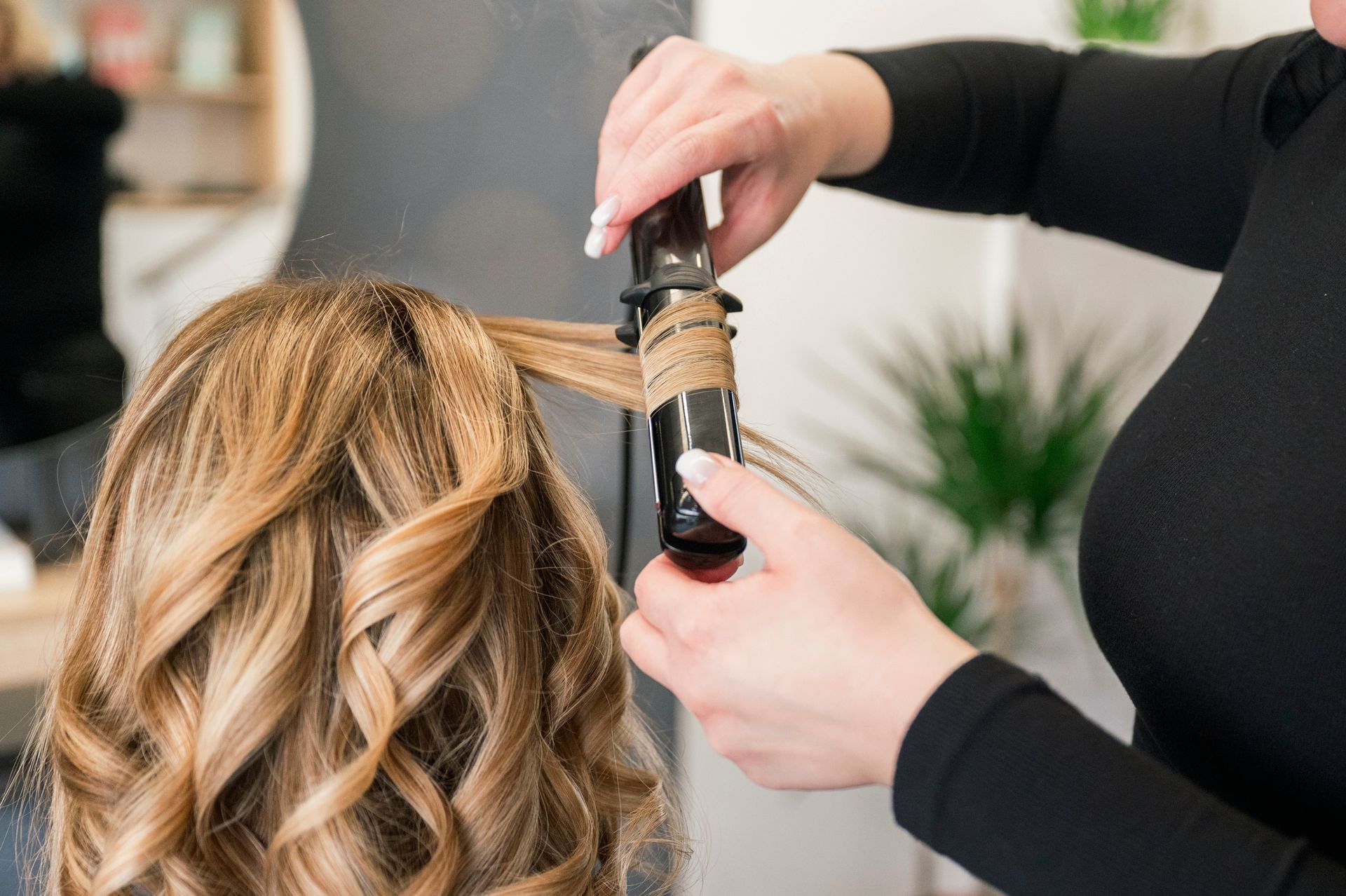 Stylist curling blonde hair with a curling iron in a salon