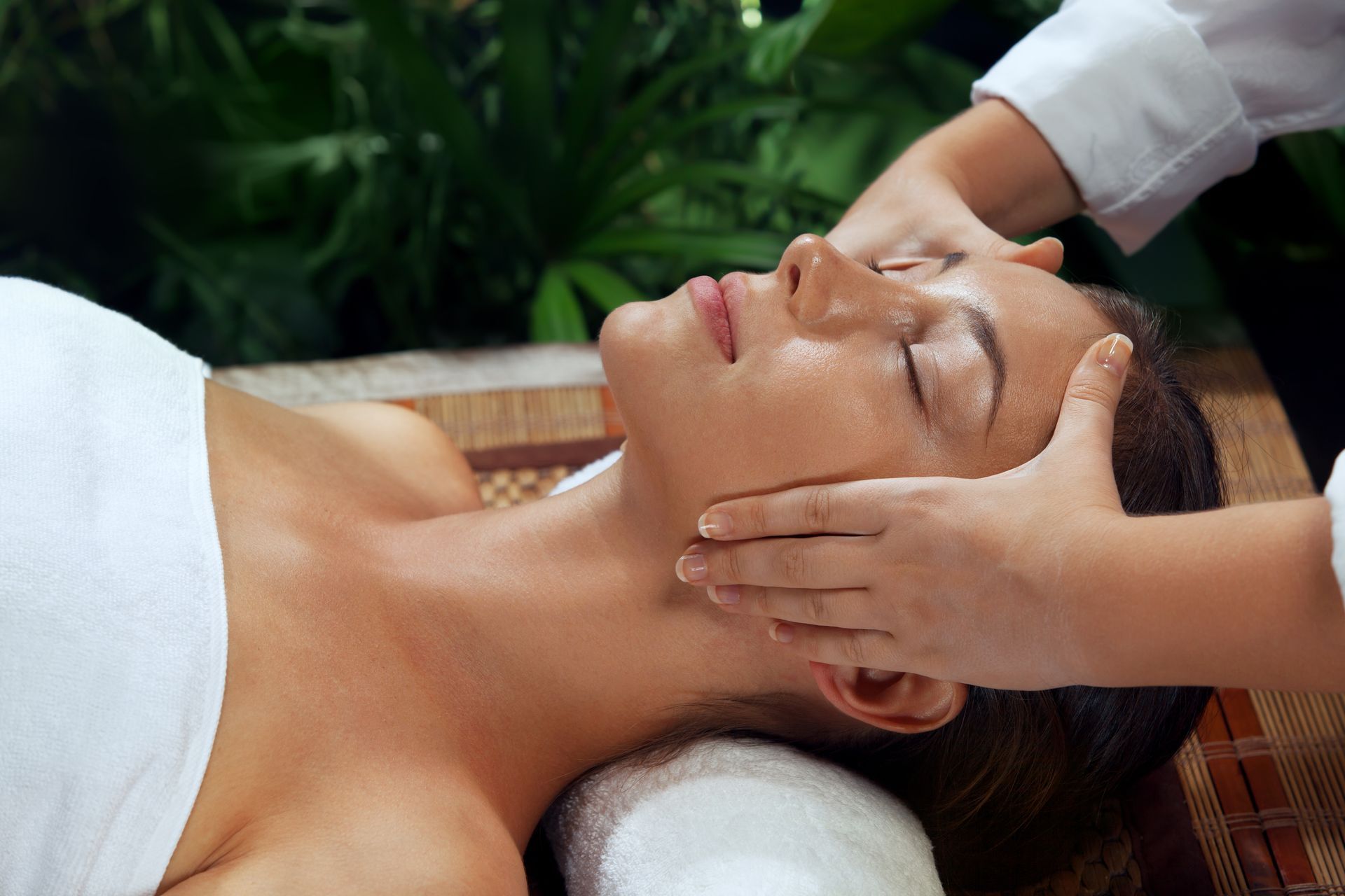 Person receiving a facial massage while lying on a towel, eyes closed, in a spa setting