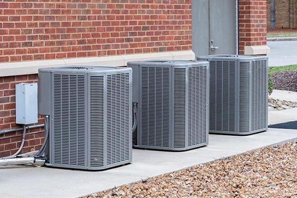 Three air conditioners are sitting outside of a brick building.