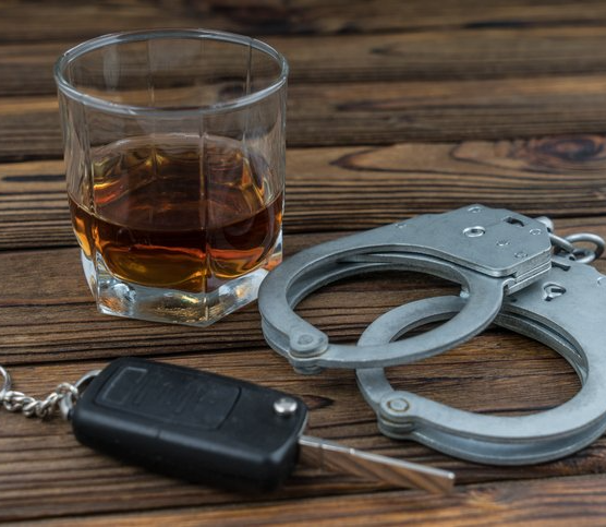 A glass of alcohol with car keys and handcuffs