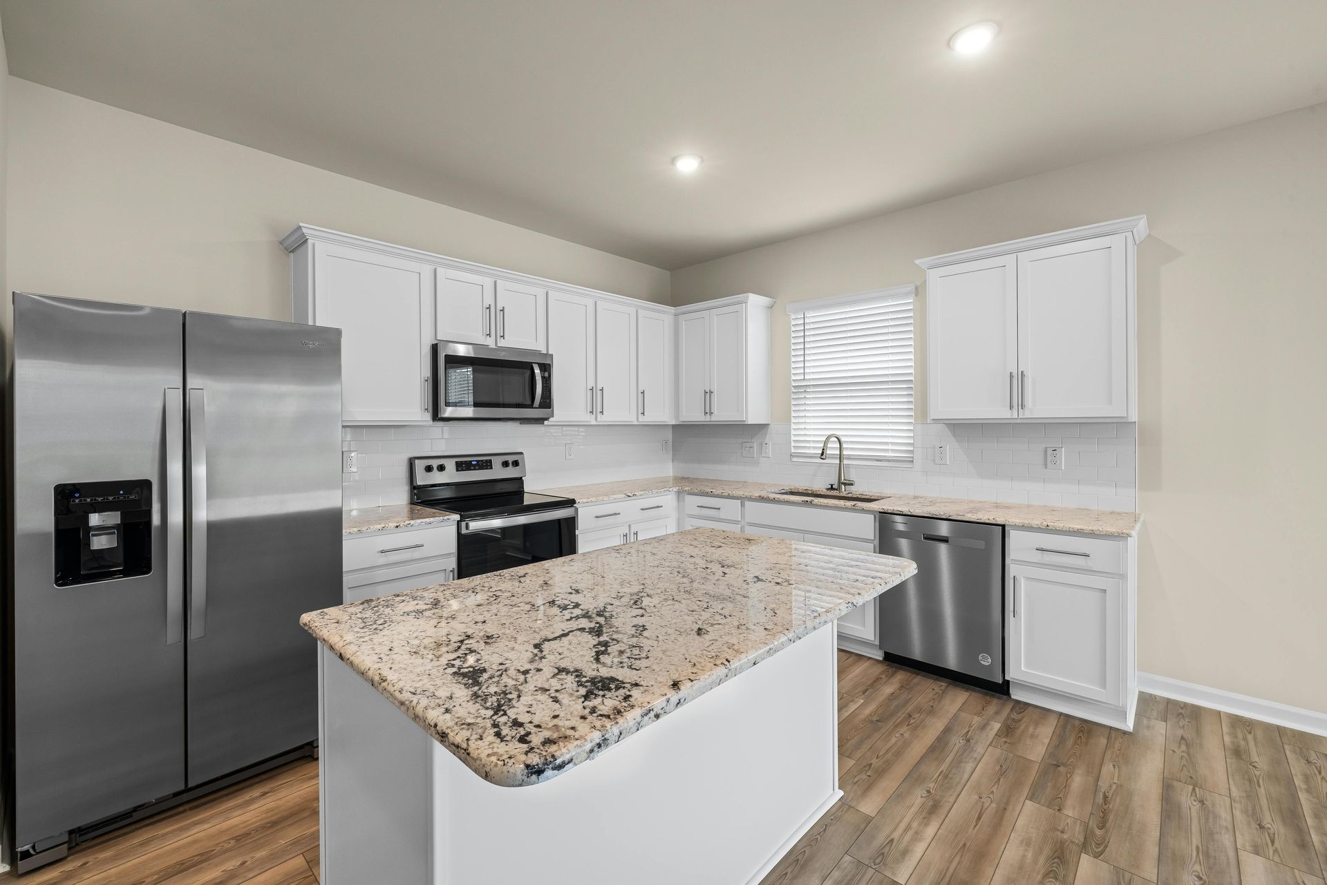 A modern kitchen featuring white cabinets, a large marble island with a sink, a stainless refrigerator, and a gas stove.