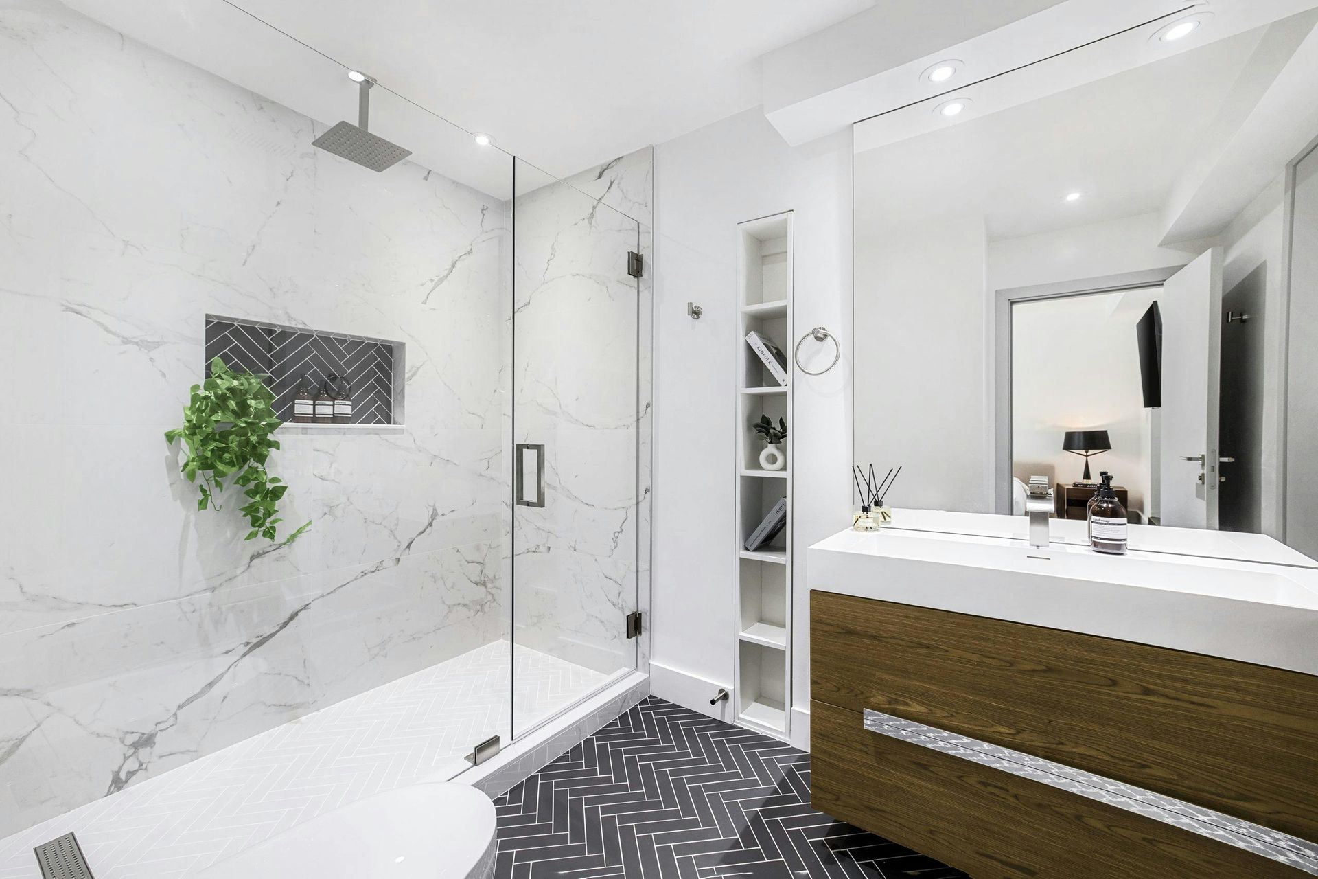 A modern bathroom with a glass-enclosed shower, white marble walls, a wooden vanity, and patterned black and white tile.
