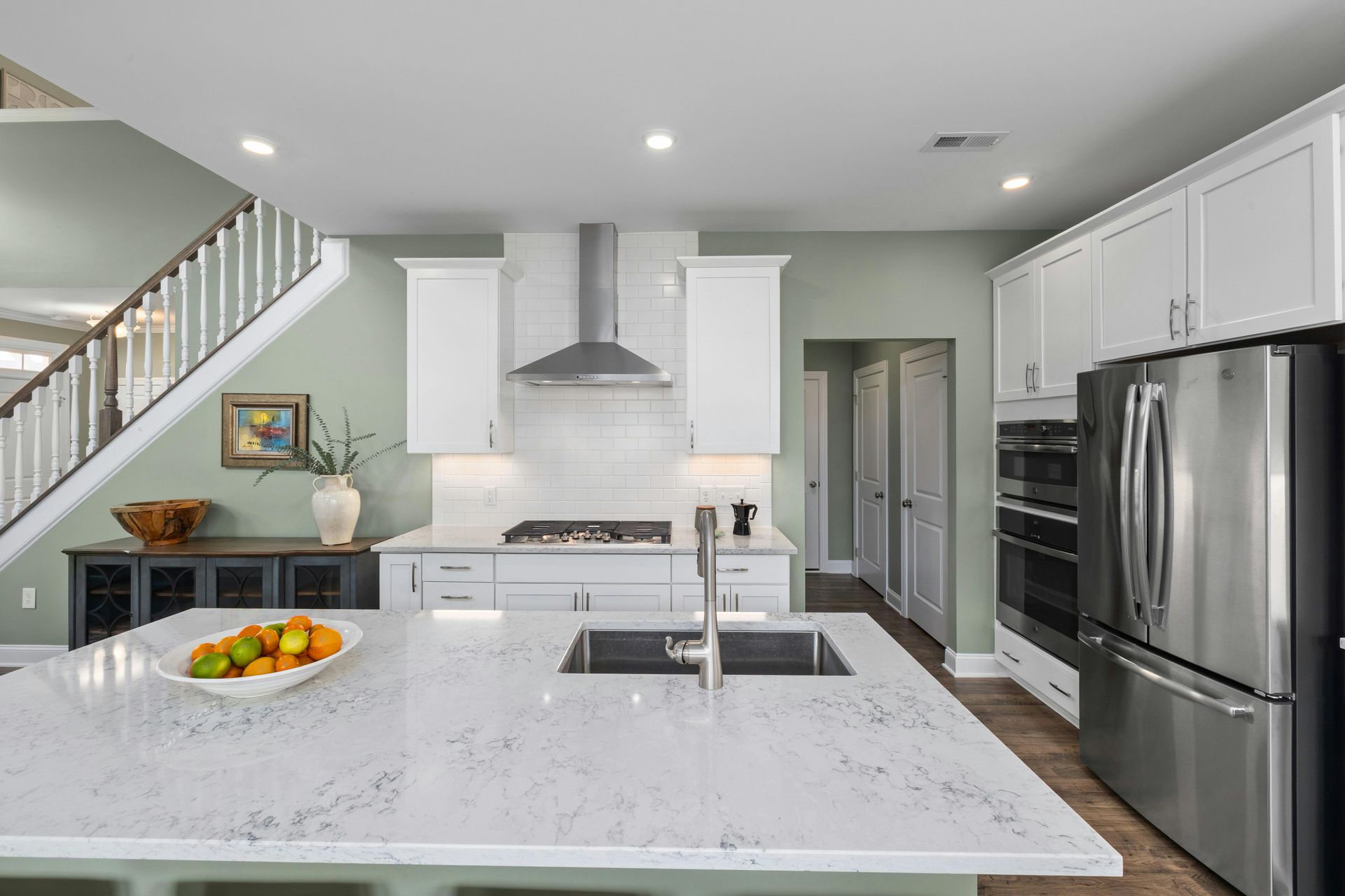 A modern kitchen featuring grey cabinets, a stainless steel hood, gas range, white subway tile backsplash, and wood floors.