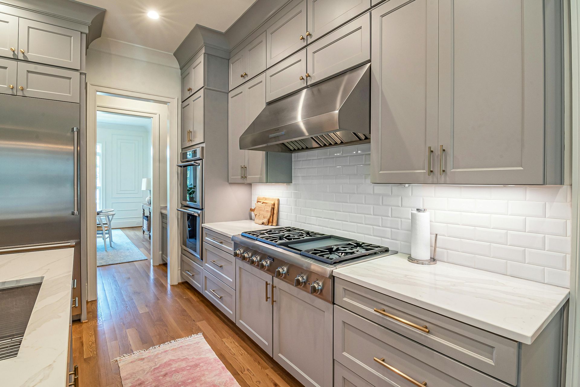 A kitchen with grey cabinets, a stainless steel range hood, a subway tile backsplash, and light countertops.