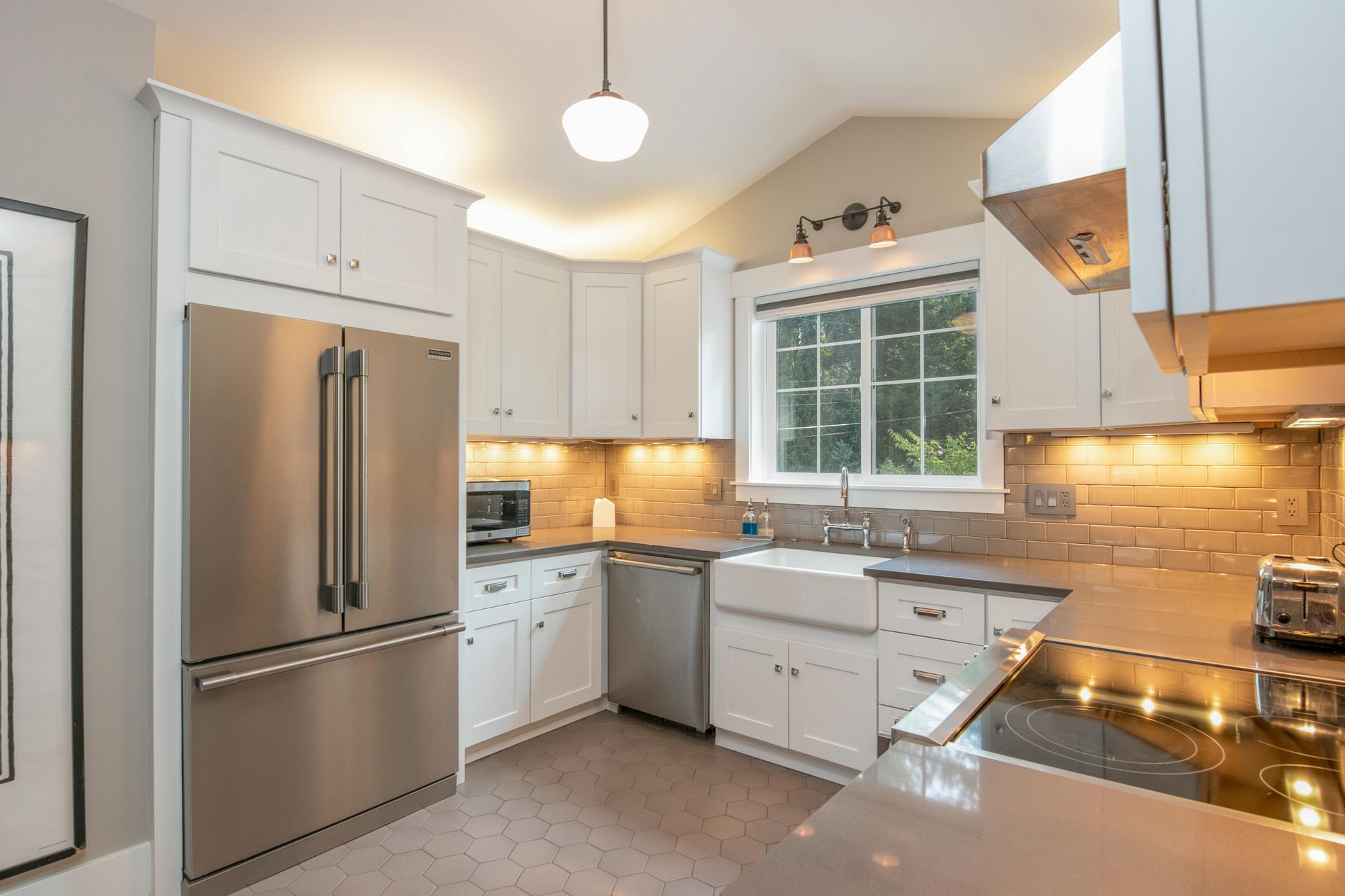 A bright, modern kitchen with white cabinets, stainless steel appliances, a farmhouse sink, and under-cabinet lighting.