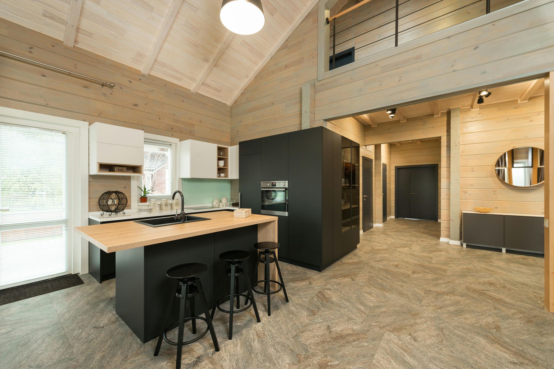 Modern kitchen with light wood walls, black island, bar stools, and a loft area in a spacious, open-concept home interior.
