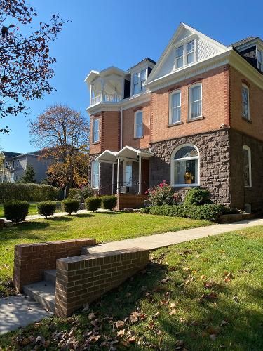 Brick building with stone base, front steps, and manicured lawn under a blue sky.