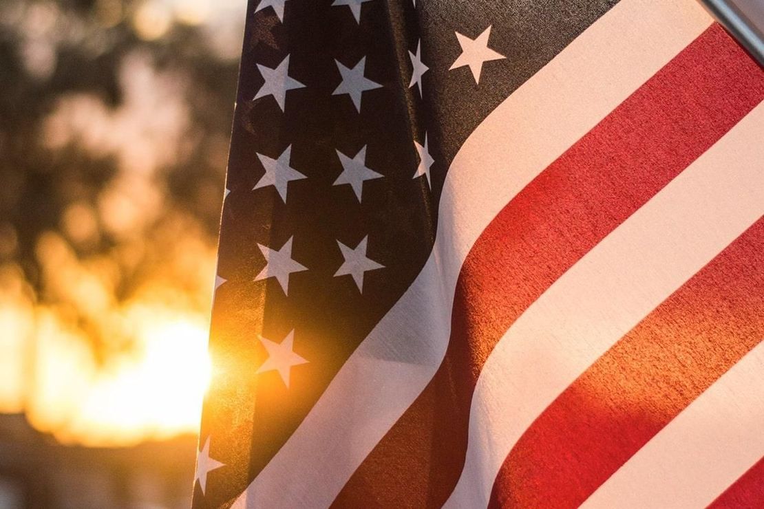 American flag with red and white stripes and white stars, backlit by a bright sunset.