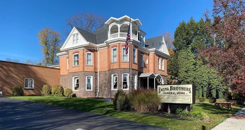 Brick building with sign for Loving Funeral Home, with a flagpole and foliage.