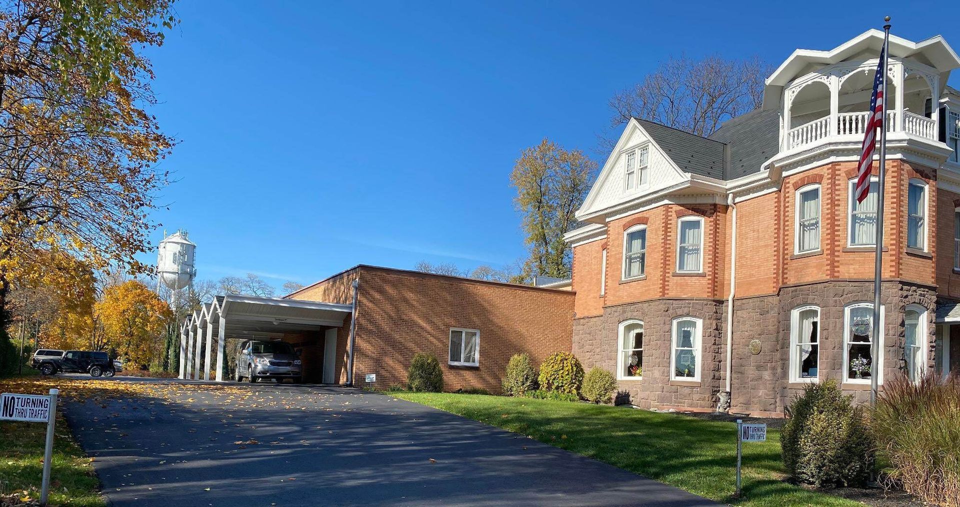 Brick building with tower and American flag, driveway, trees, and blue sky.