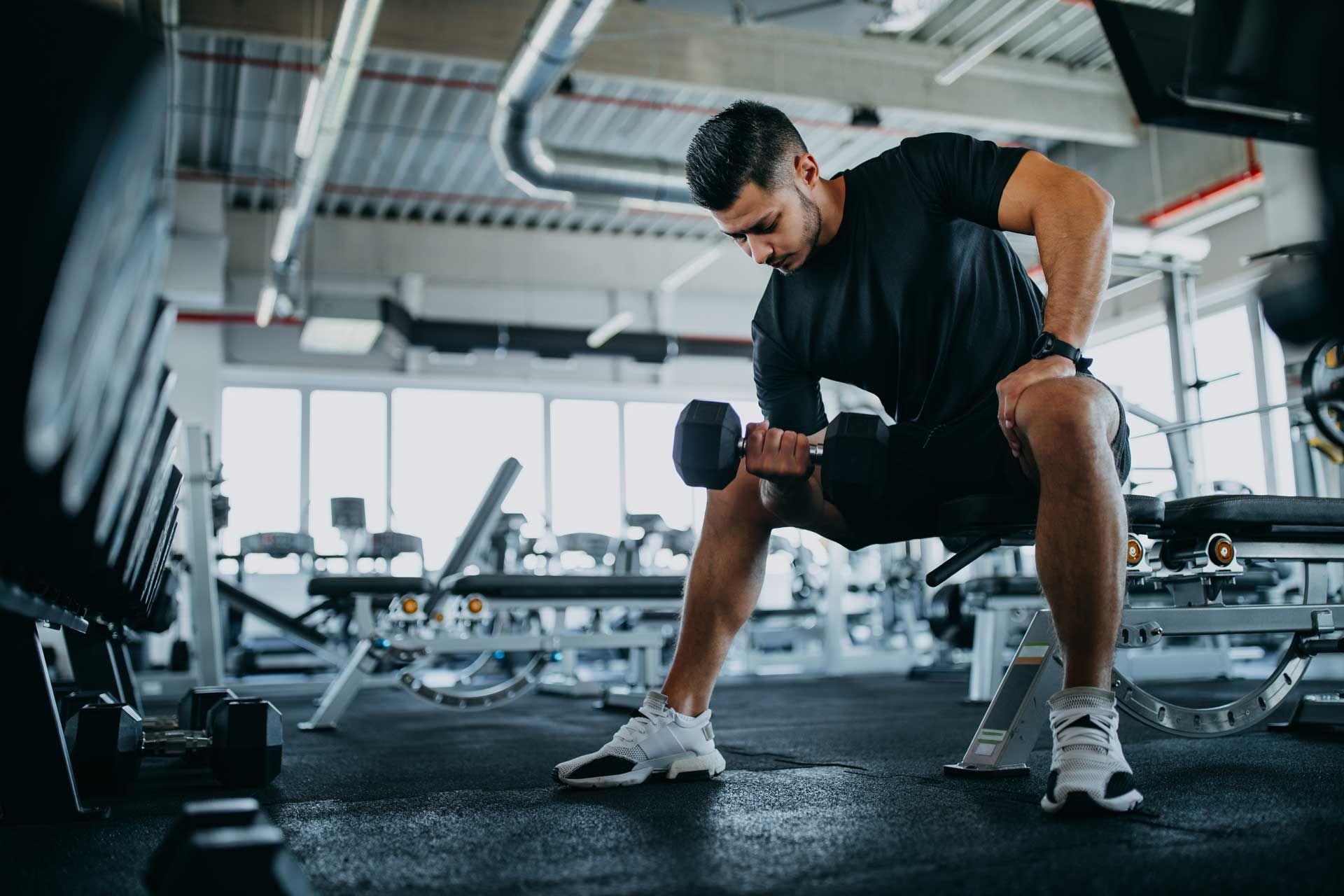 A man is sitting on a bench in a gym holding a dumbbell.