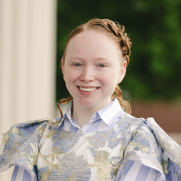 Smiling person in a silver patterned top, standing outdoors with a blurred green background