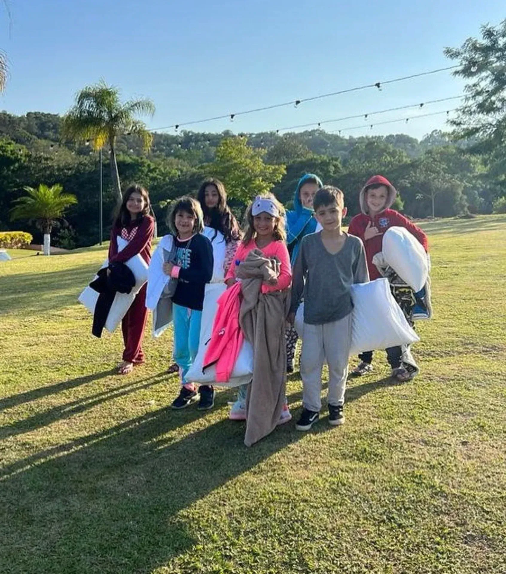 um grupo de crianças está em um campo gramado segurando travesseiros.