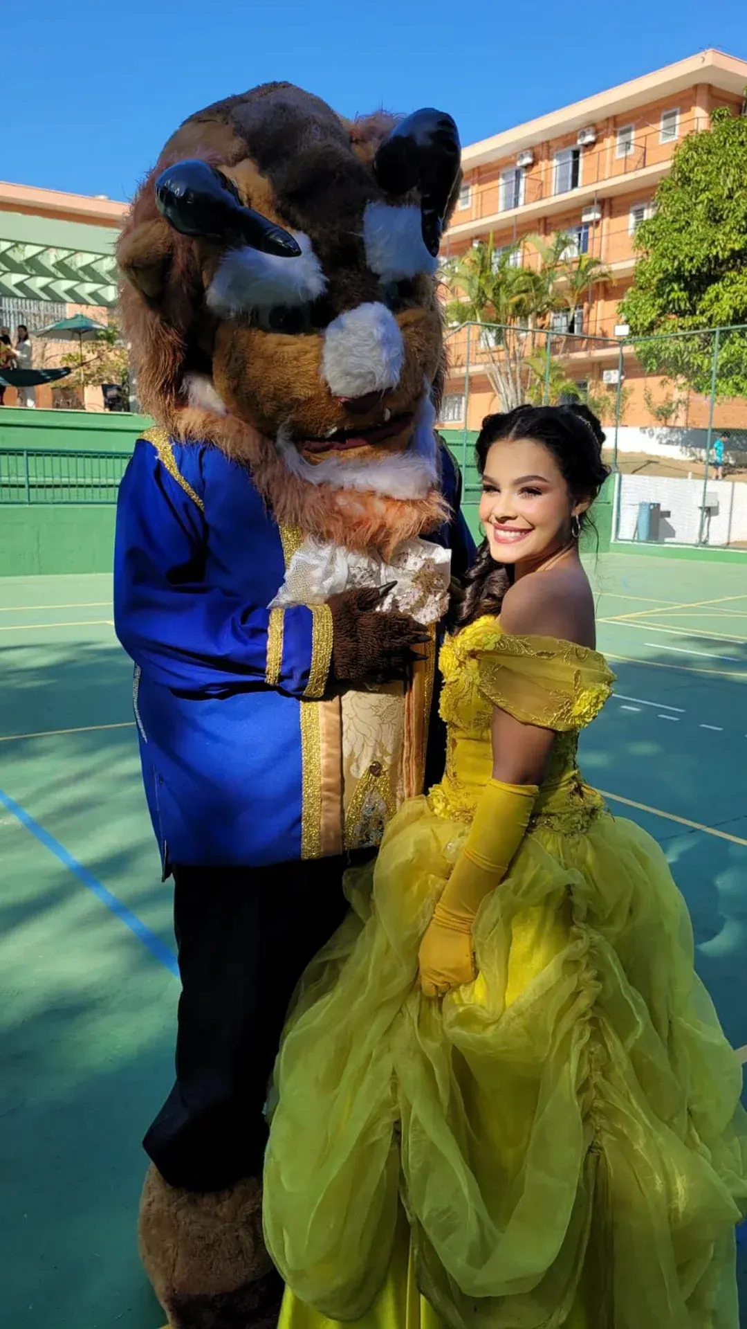 uma mulher de vestido amarelo está parada ao lado de um mascote vestido de fera.
