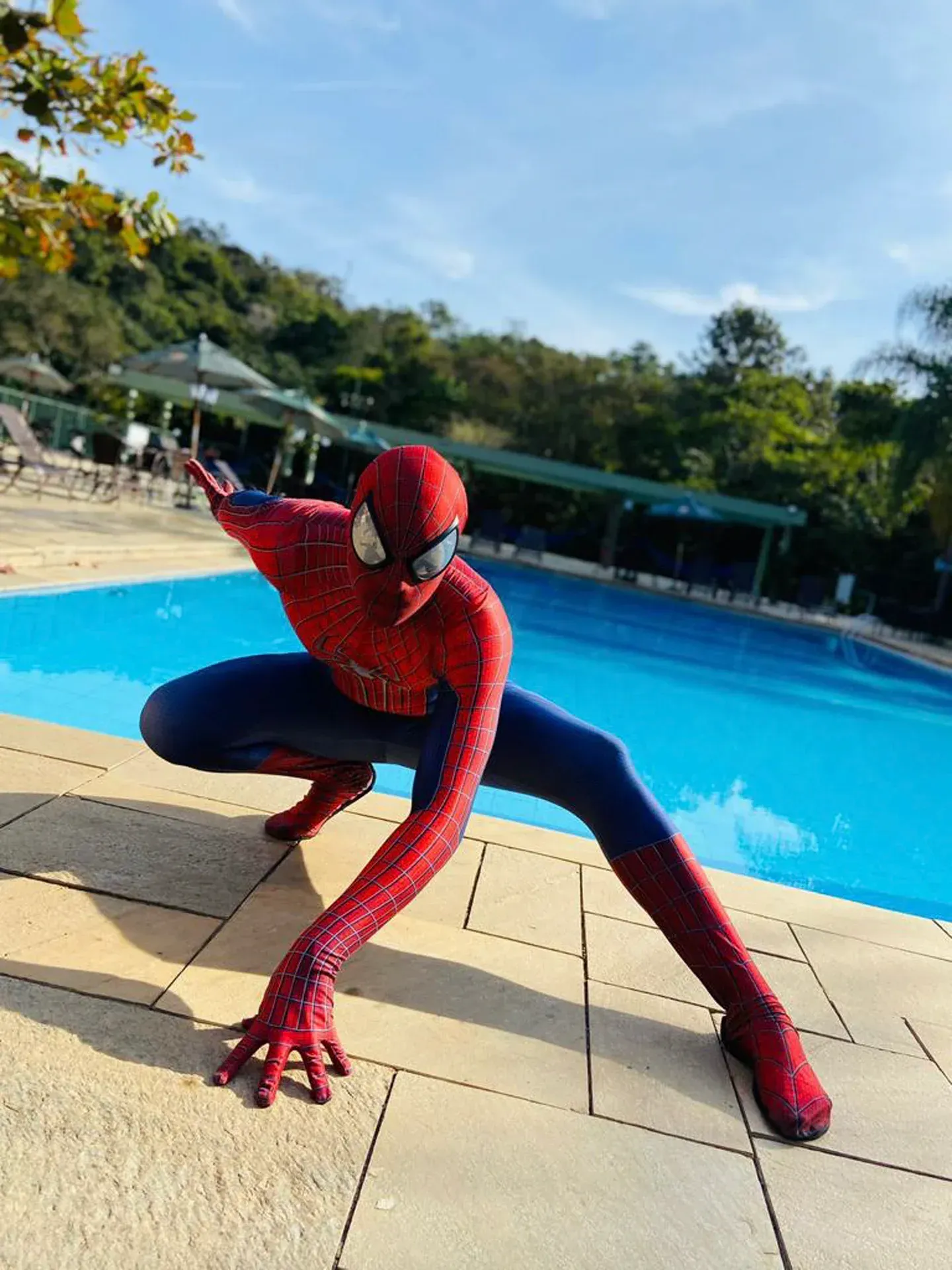 um homem fantasiado de homem-aranha está ajoelhado ao lado de uma piscina.