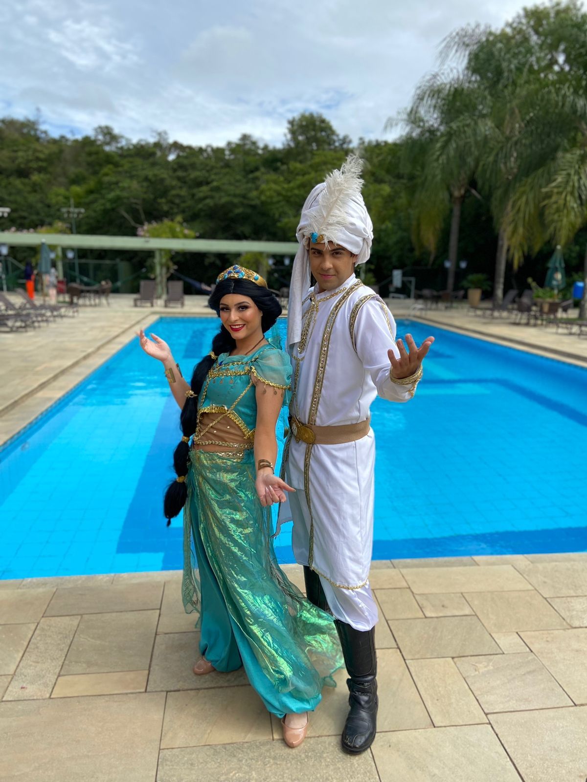 um homem e uma mulher fantasiados estão parados ao lado de uma piscina.