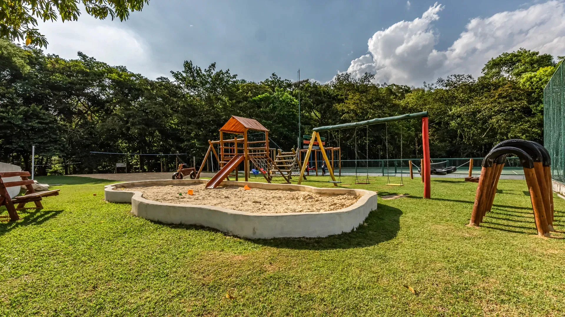 um playground com caixa de areia e balanços em um parque.