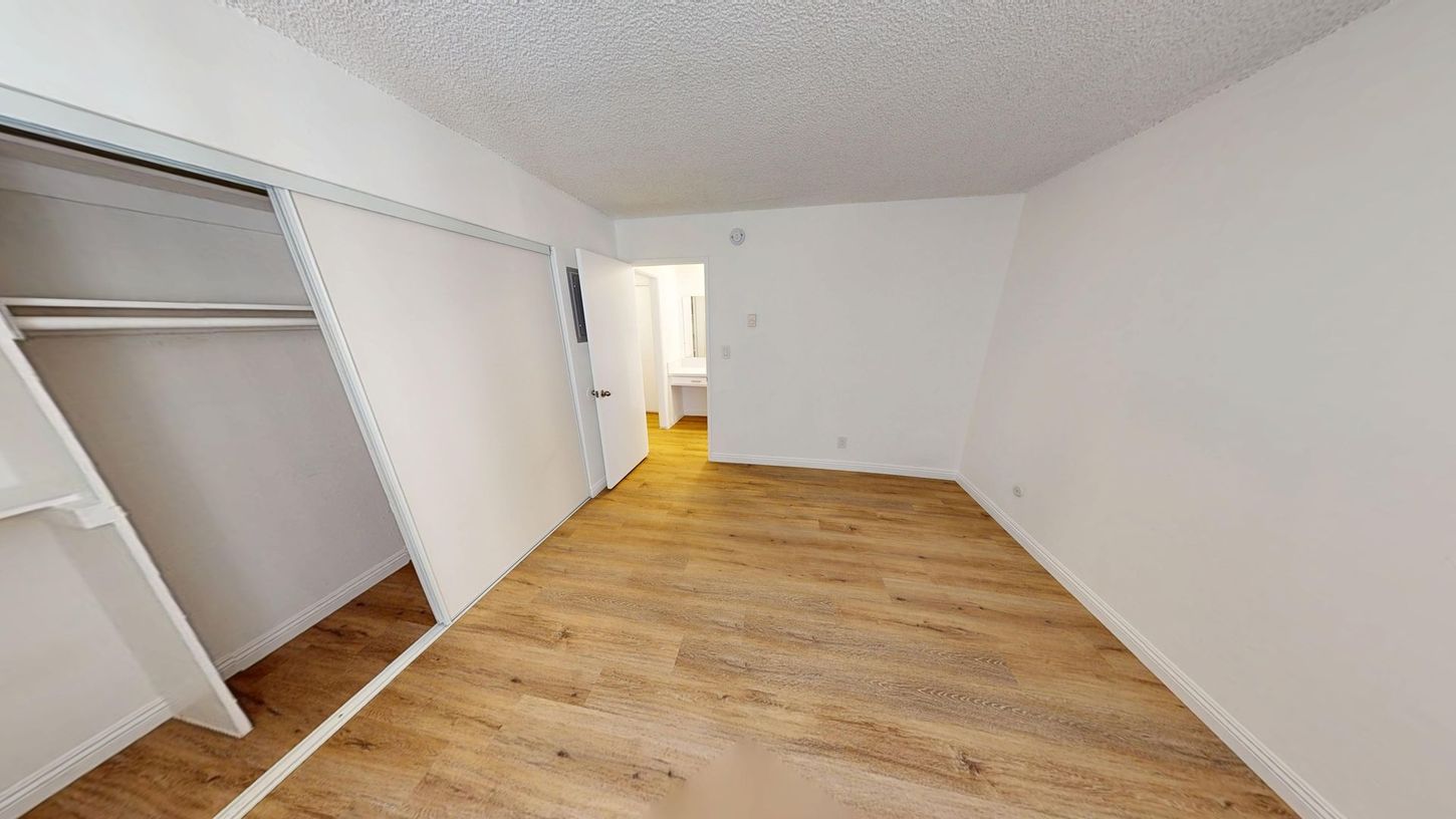 Empty bedroom with closet and doorway to bathroom. Wooden floor, white walls.