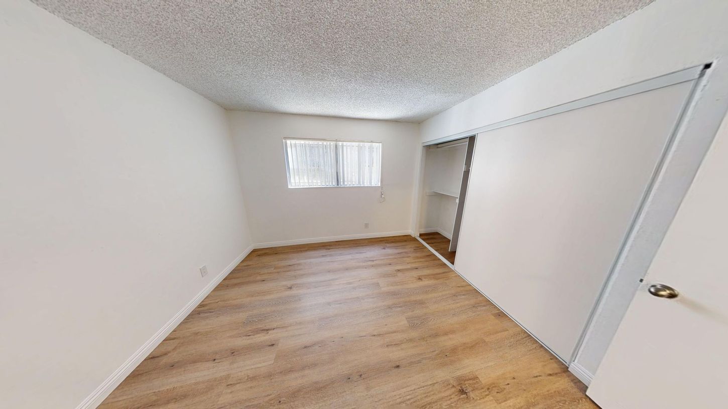 Empty bedroom with wood-look flooring, white walls, small window, and closet.