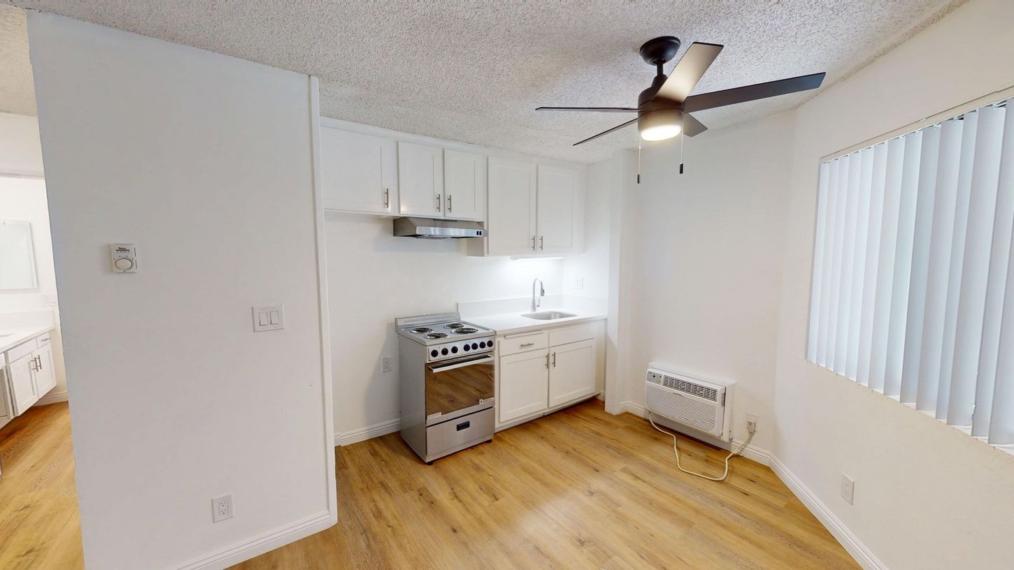 Small kitchen with white cabinets, stove, sink, and a ceiling fan.