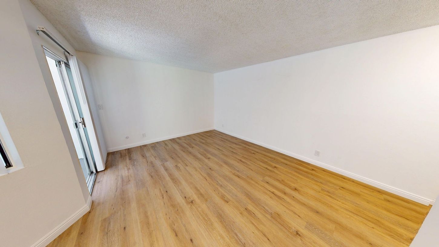 Empty room with light wood floors, white walls, and a sliding glass door.