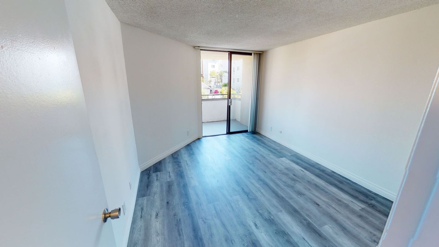 Empty room with light blue wood-like floors, white walls, and a glass door to a balcony.