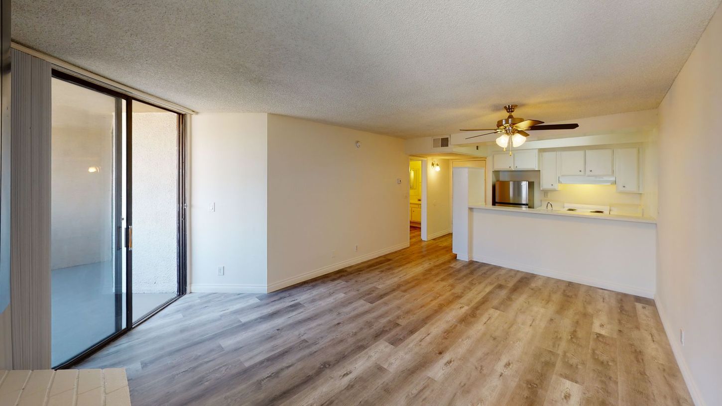 Spacious living area with sliding glass doors, wooden floors, and kitchen visible in the back.