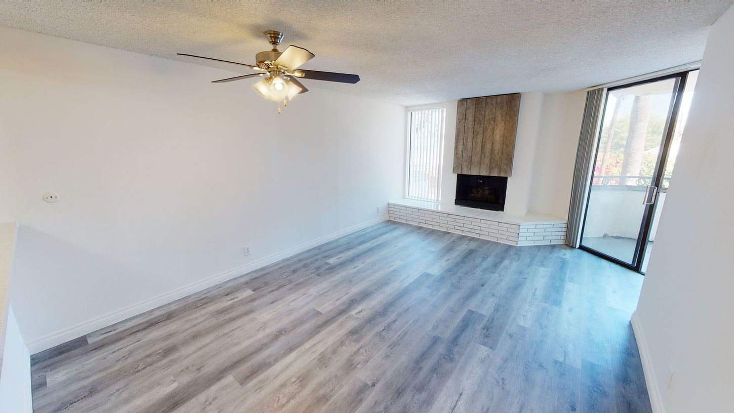 Empty living room with wood-look floor, white walls, fireplace, and sliding glass door to balcony.