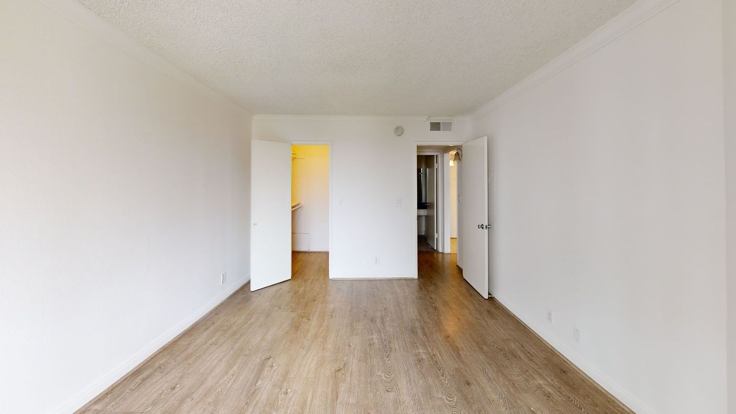 Empty room with light wood floors, white walls, and open doorways to other rooms.