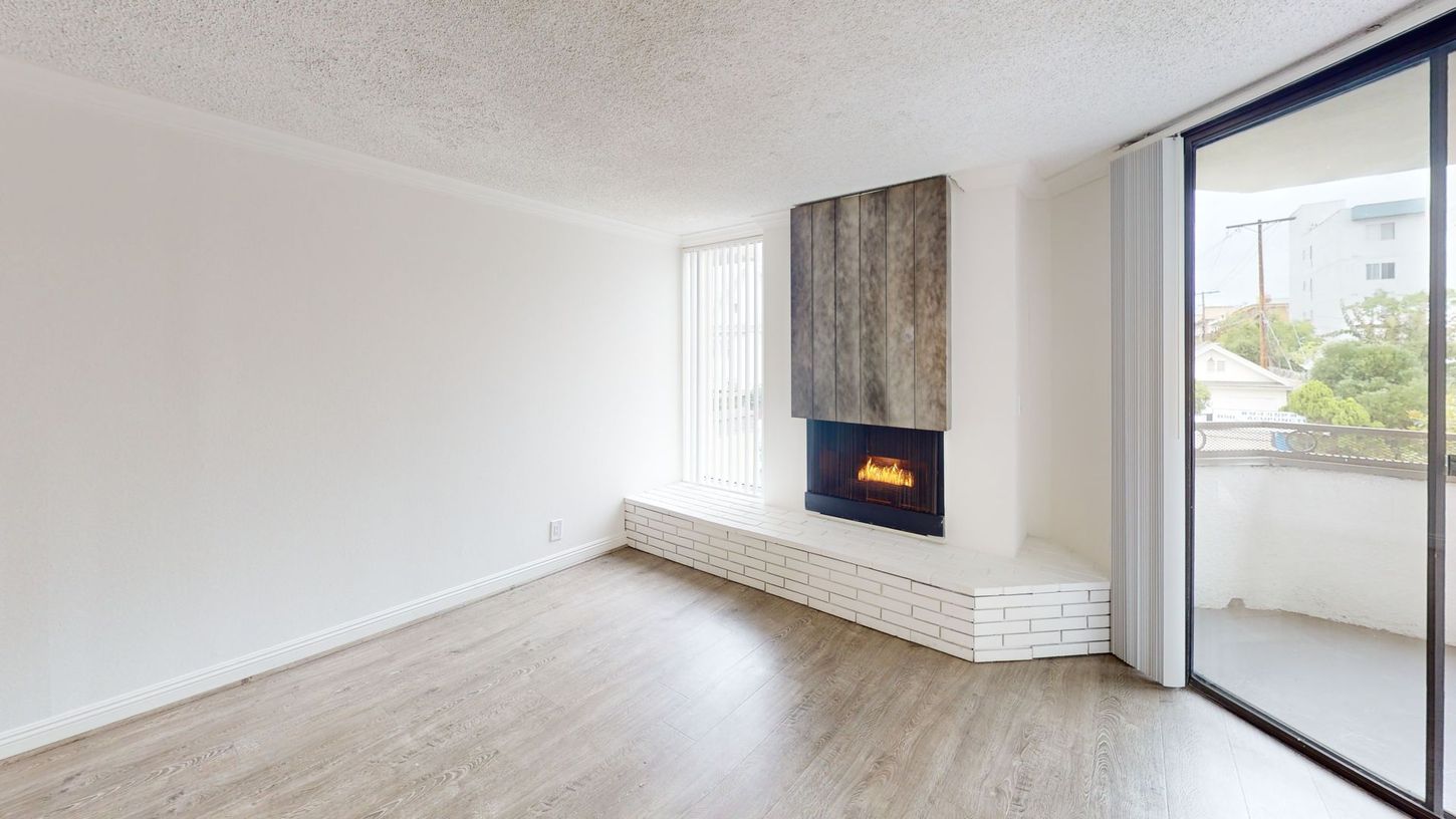 Empty living room with fireplace, white walls, and balcony access.