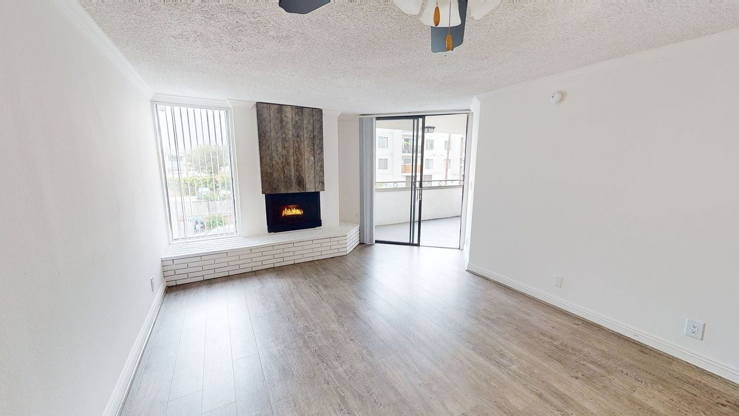 Living room with fireplace, sliding glass door, white walls, and wood-look flooring.