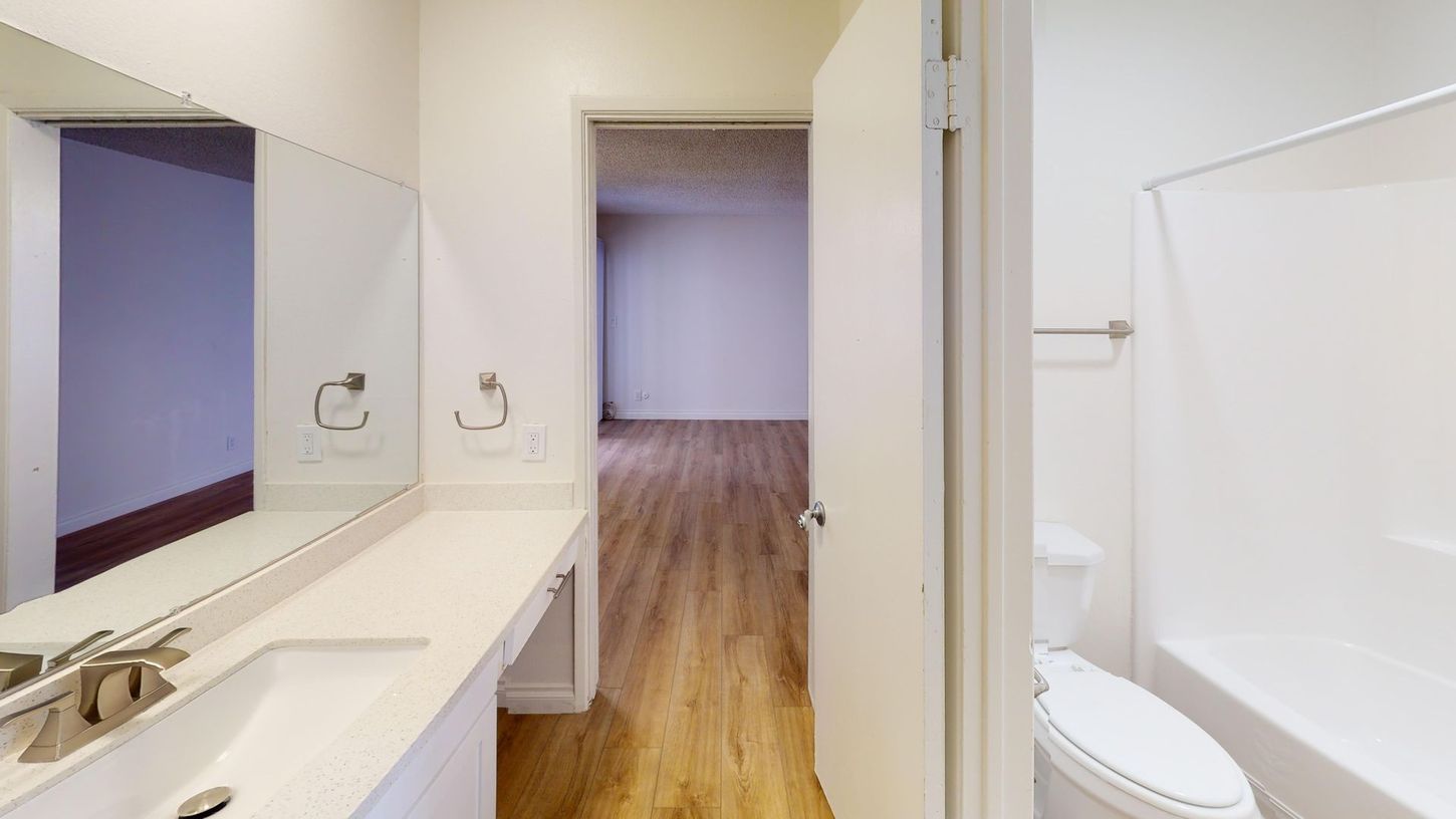 Bathroom with open door to a room with wood floors. Includes a sink, mirror, and toilet.