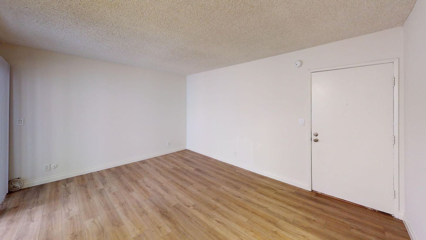 Empty room with light wood flooring, white walls, and a white door.