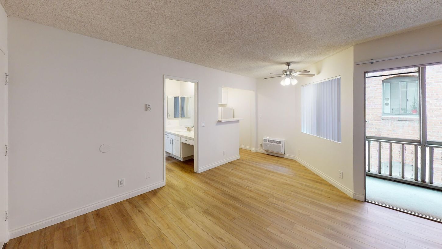 Interior view of a small apartment with hardwood floors, a bathroom, and a sliding glass door to a balcony.