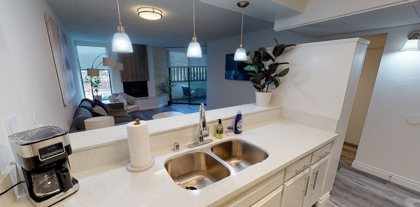 Kitchen interior with a double sink, coffee maker, and view into the living room.