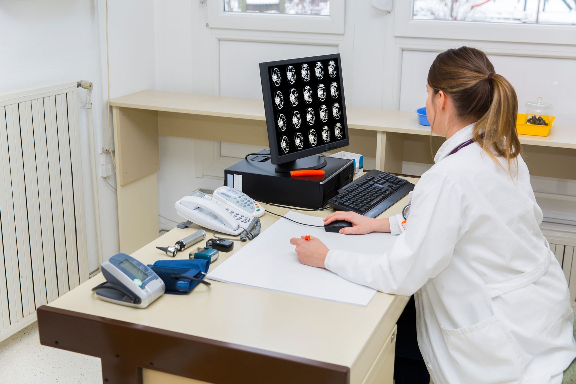A female doctor is sitting at a desk in front of a computer.