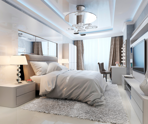 Bright modern bedroom with a neatly made bed, white decor, and a wall-mounted TV