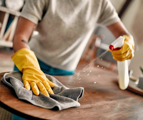 Gloved hands cleaning a wooden table with spray and cloth