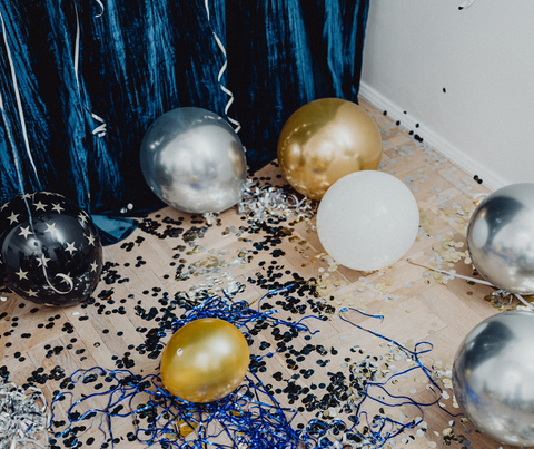 Scattered balloons and confetti on a floor with blue curtains, suggesting a celebration aftermath