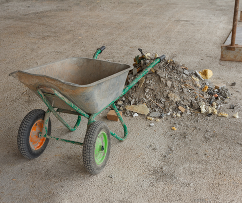 Green wheelbarrow beside a pile of rubble on a concrete floor in a construction area