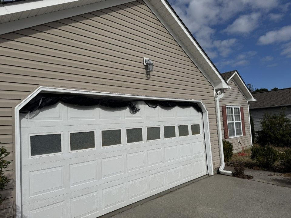 Garage door on a house with siding and a light fixture, on a sunny day.