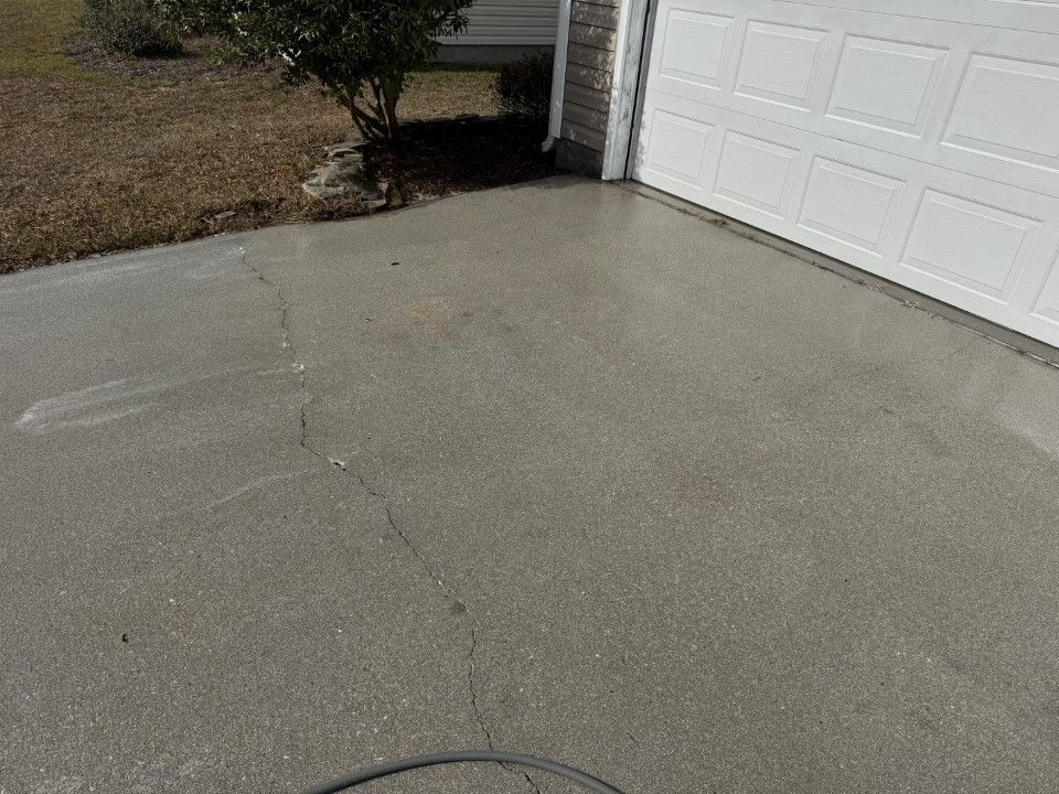 Concrete driveway with cracks, leading to a white garage door. A hose lays on the driveway.