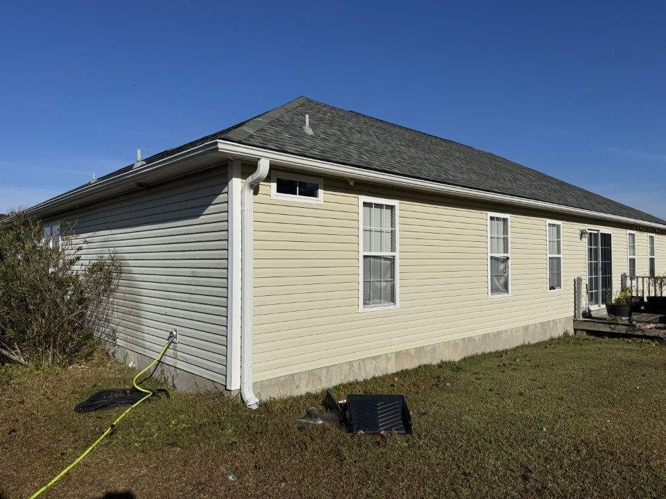 Tan and gray siding house with gray roof, windows, and gutter. Green grass and blue sky in background.