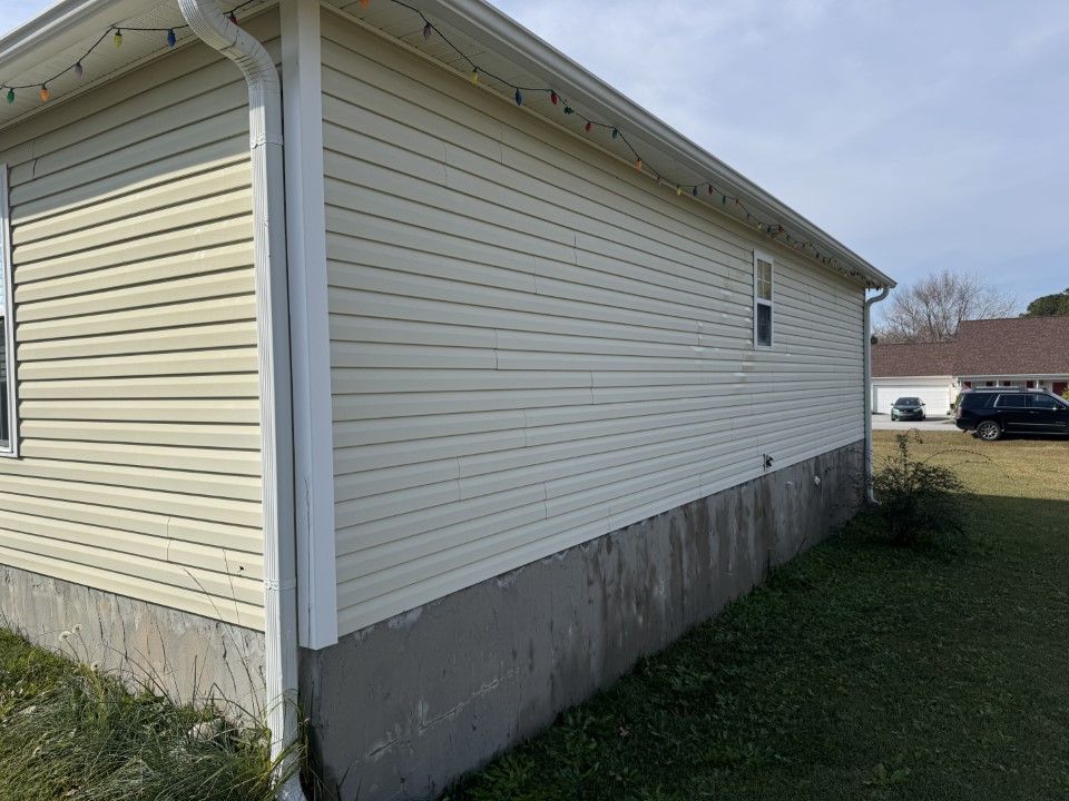 Beige vinyl-sided house with a concrete foundation. A small window is visible.