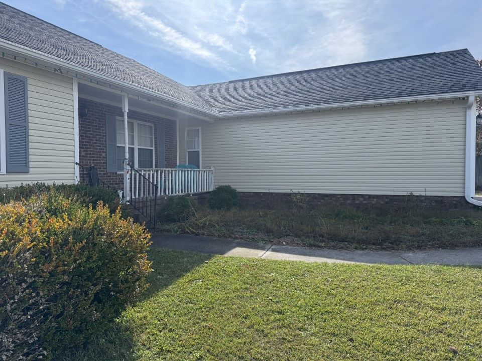 Tan house with gray roof, porch, and green lawn. Blue shutters on the side.