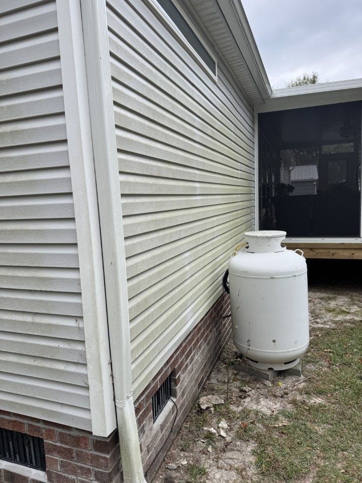 White siding on a house next to a propane tank. Brick foundation and a screened porch are also visible.